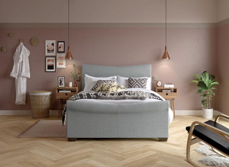 Grey ottoman bed with white winter bedding, styled against a pink wall with grey details