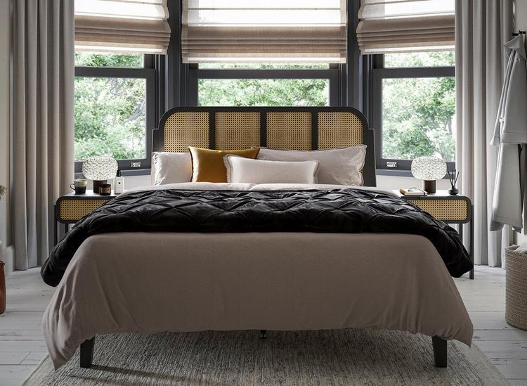 Black wooden and rattan bed frame, styled with matching bedside tables in a bay window.