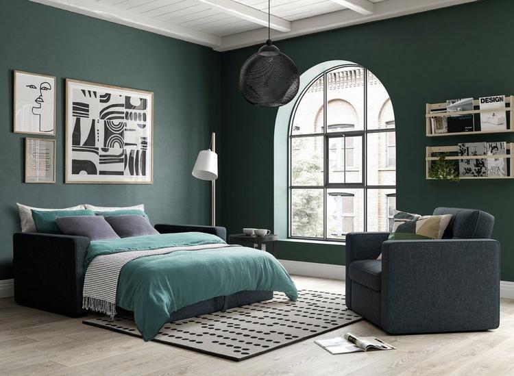 Navy blue sofa bed made up as a bed, styled in a dark green living room with matching armchair