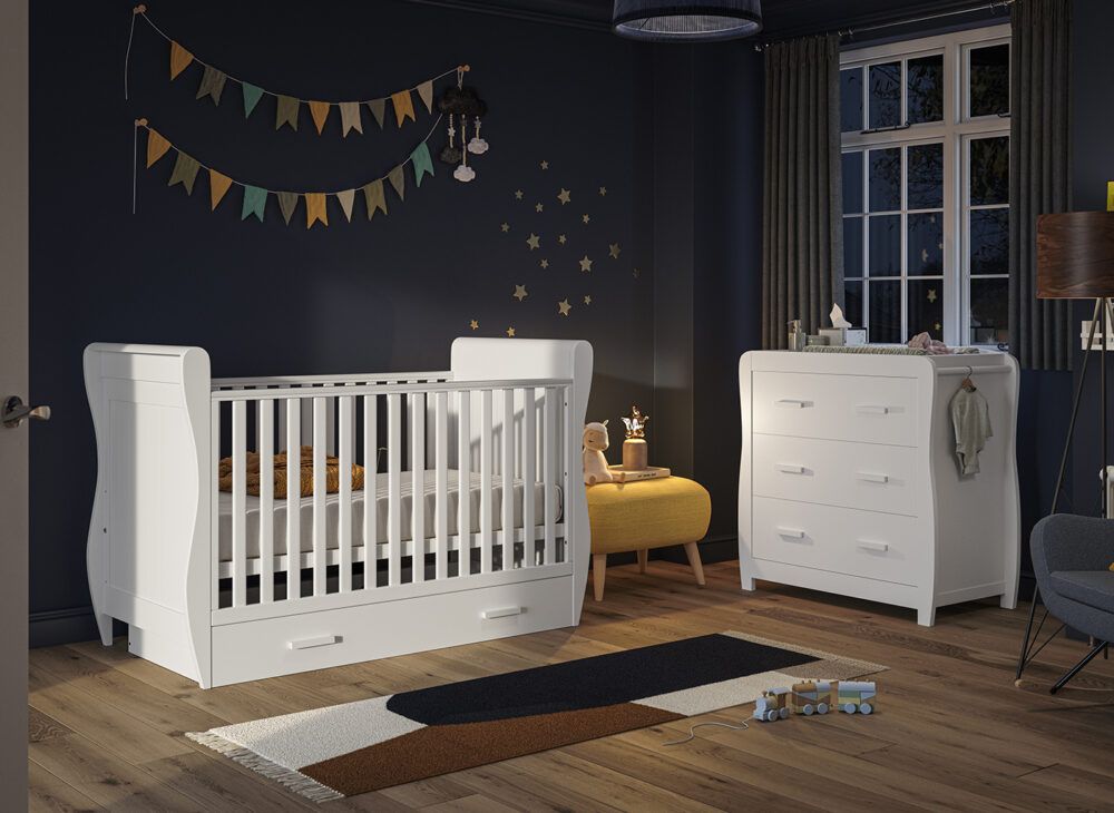 A white cot and 2-in-1 chest and changing station, dressed in dark cosy nursery with wall decor.