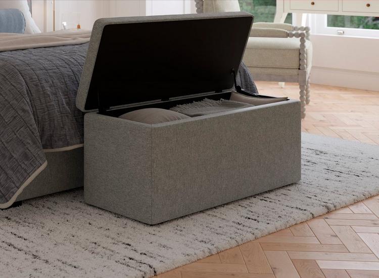 Grey soft touch blanket box with buttoned details sat open at the foot of a bed