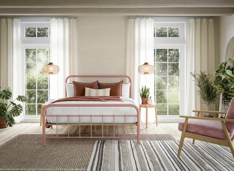 Pink metal bed frame in a neutral room with green plants