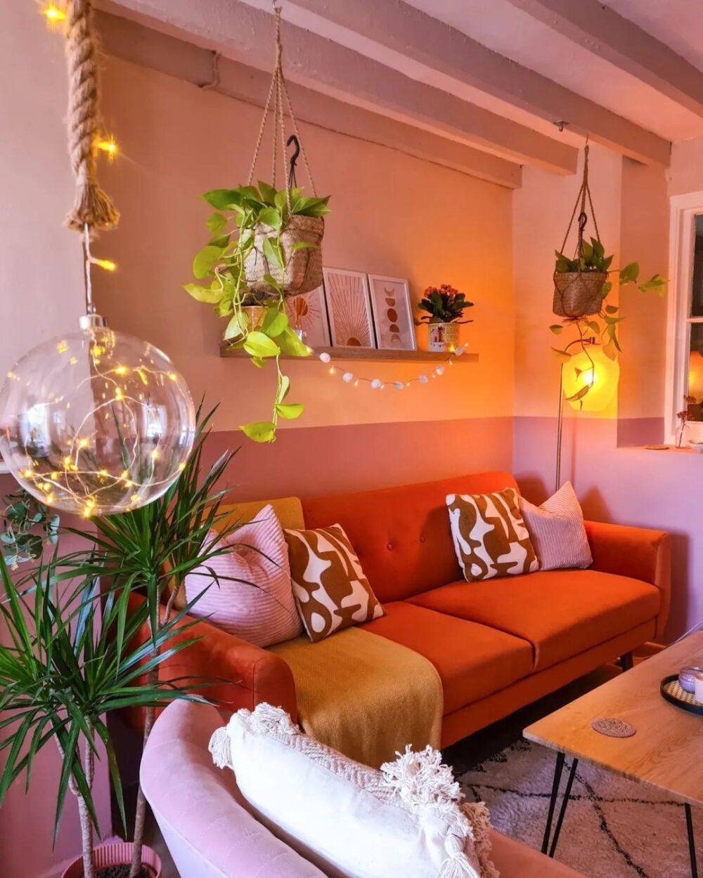 Bright orange sofa bed, styled against a pink colour blocked walls with botanical accents and feature lighting.