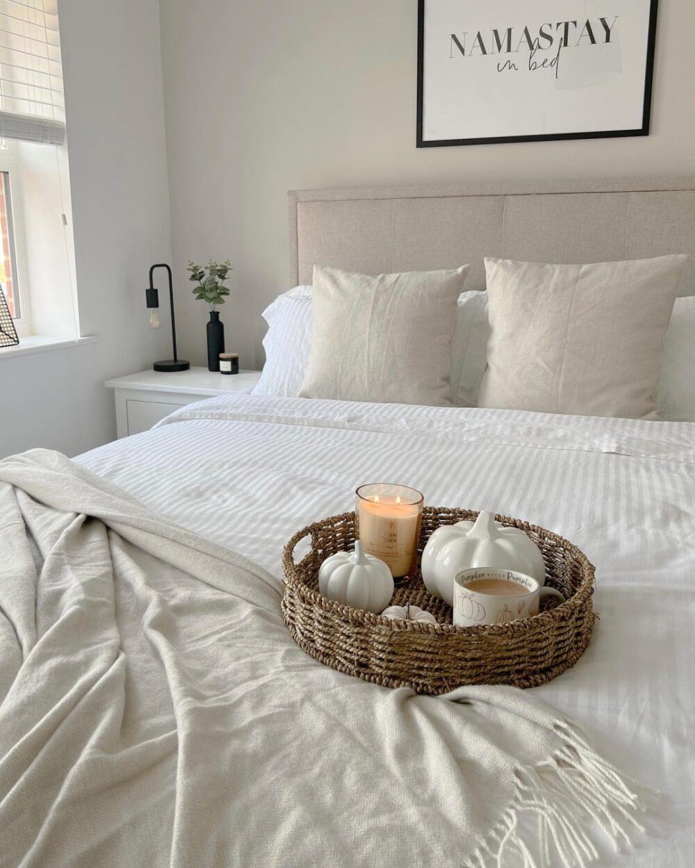 A beige upholstered bed frame, styled with white bedding