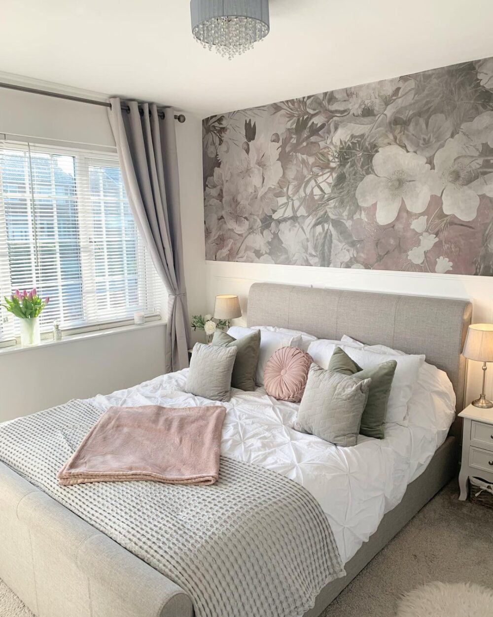 blush pink cushions on white bedding and grey bed with a floral mural of grey, pink and white.