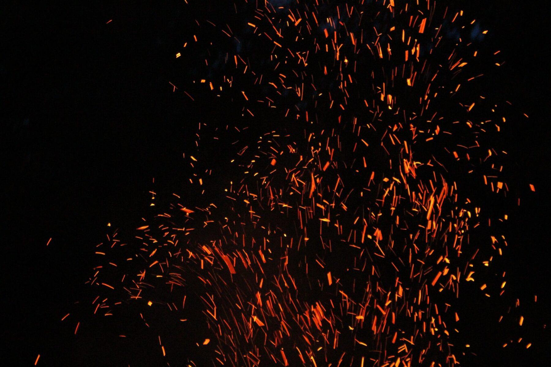 image of embers of a fire spitting up against a dark black sky