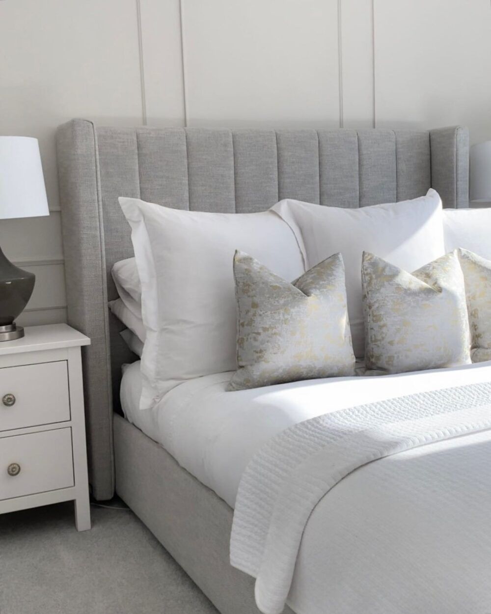 A grey upholstered bed frame, styled with white bedding