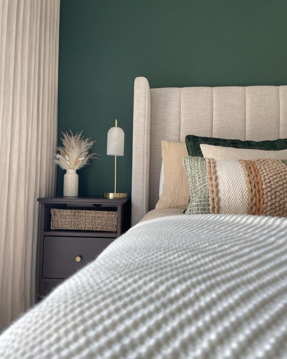 A grey upholstered bed frame, styled in a dark green bedroom