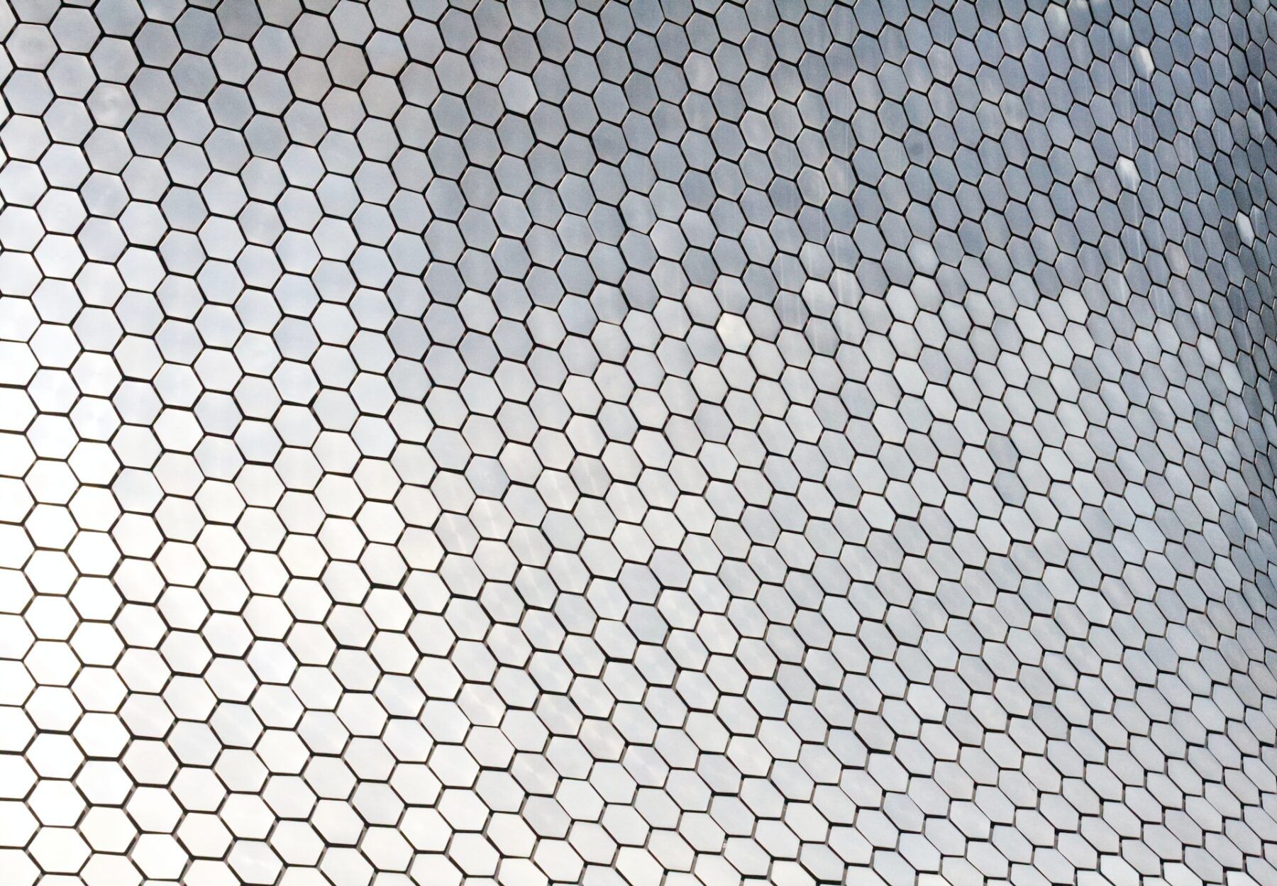 abstract image of a zoomed in building which is made up of small metallic hexagons creating a modern honeycomb with a gradient from shiny whites to darker, shadowed greys