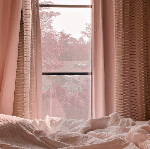 pink bedroom with light pink bedding and pink curtains and an autumnal, tree-lined scene visible through the window