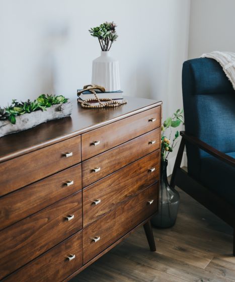 tall dresser in small bedroom with plant on top and chair to the side