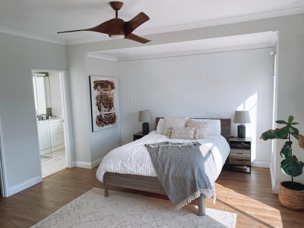 A low-rise wooden bed frame, styled in a neutral white room with wooden accents