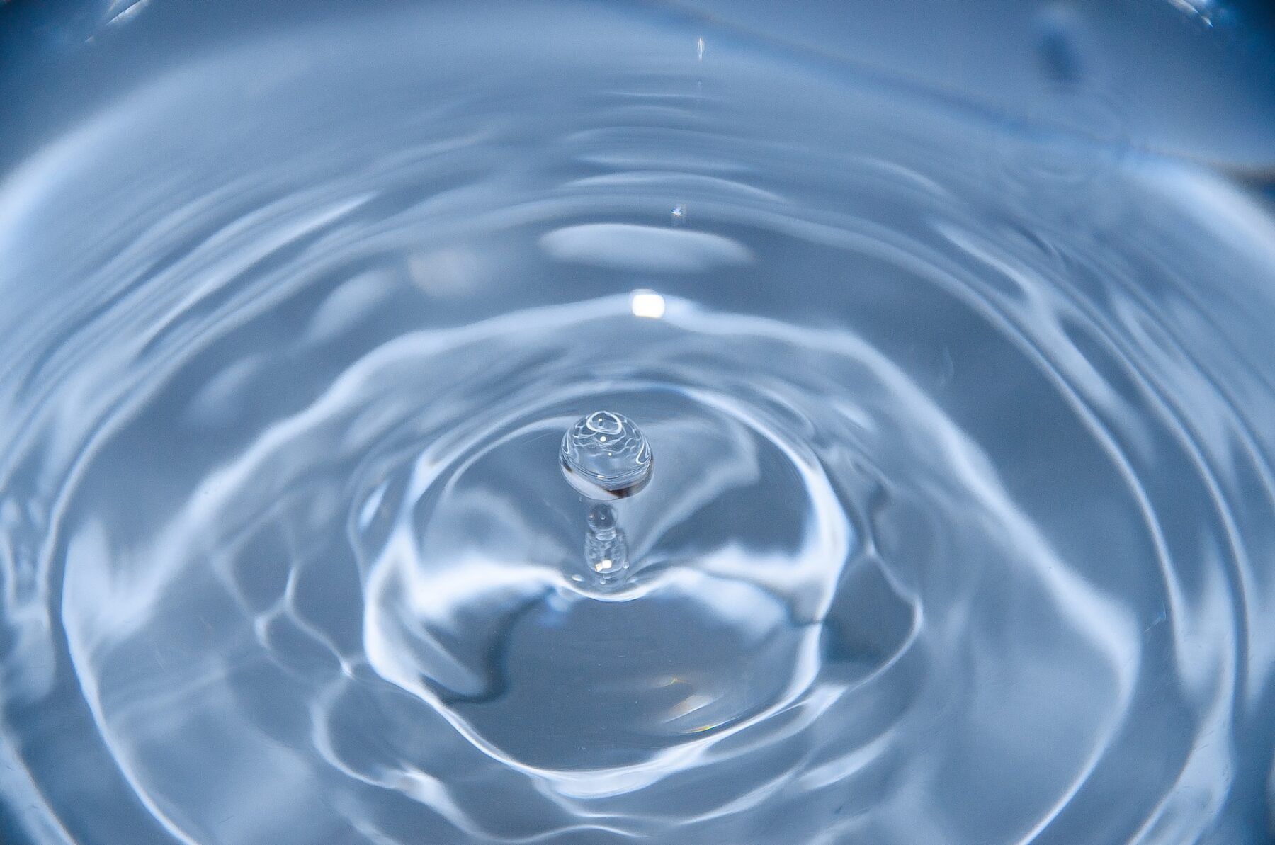 zoomed in image of water where a drop is about to fall on the surface. Previous drops have caused a ripple effect towards the wider edge of the image.