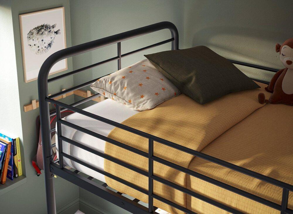 view of the top bunk of a metal bunk bed with mustard bedding and textured sheets and pillows against a dark green backdrop.