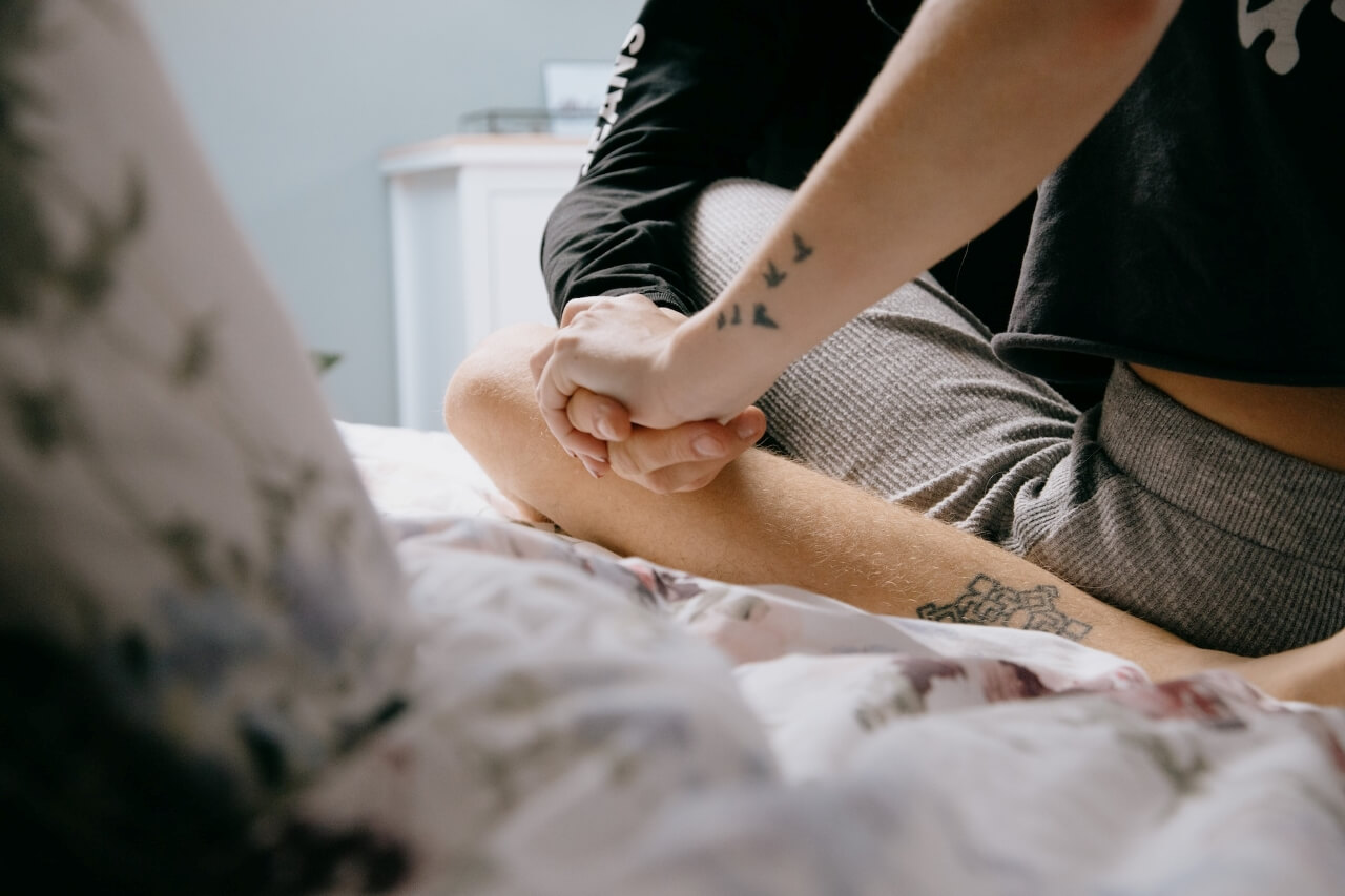 Close-up of couple holding hands sat on bed