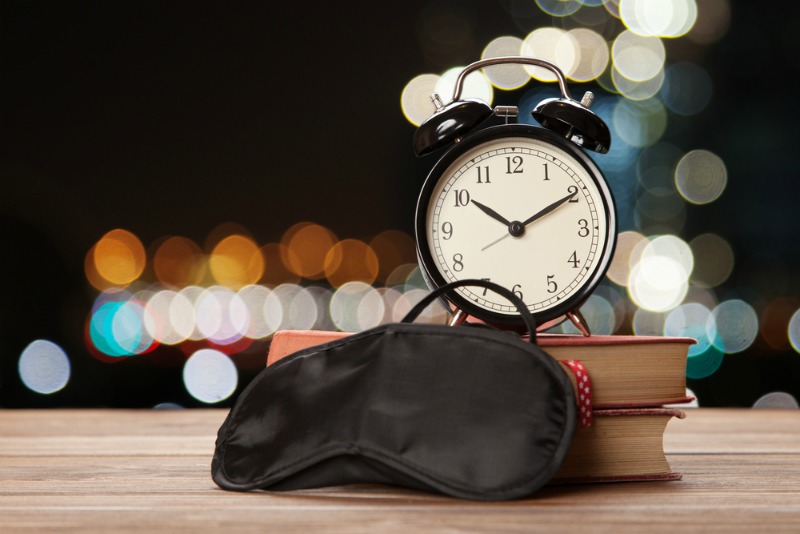 An image showing a sleeping mask, books and alarm clock