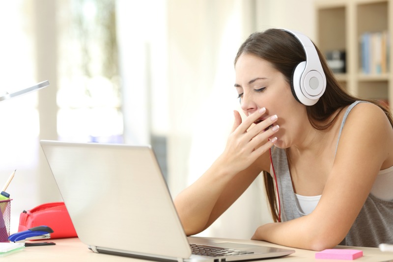 Women is yawning in front of laptop wearing white headphones.