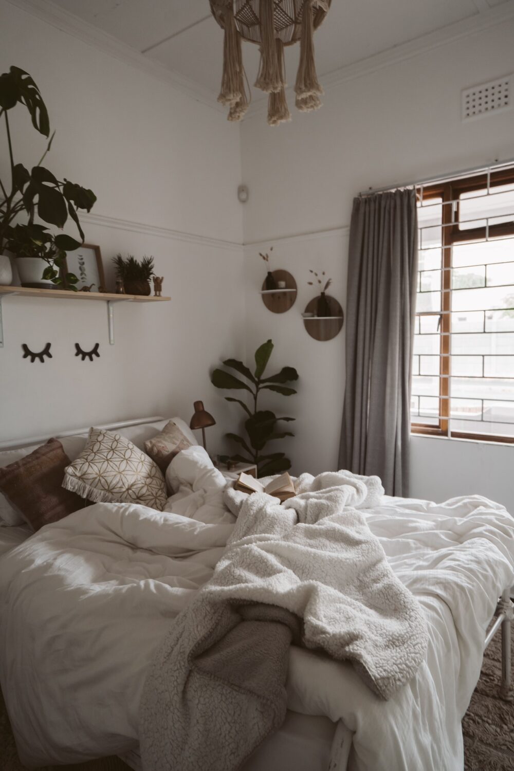 A white and plant filled bedroom is filled with natural light from the windows.