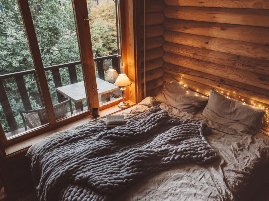 hygge bedroom to show hygge decor with chunky knitted throw, pillows and warm lighting