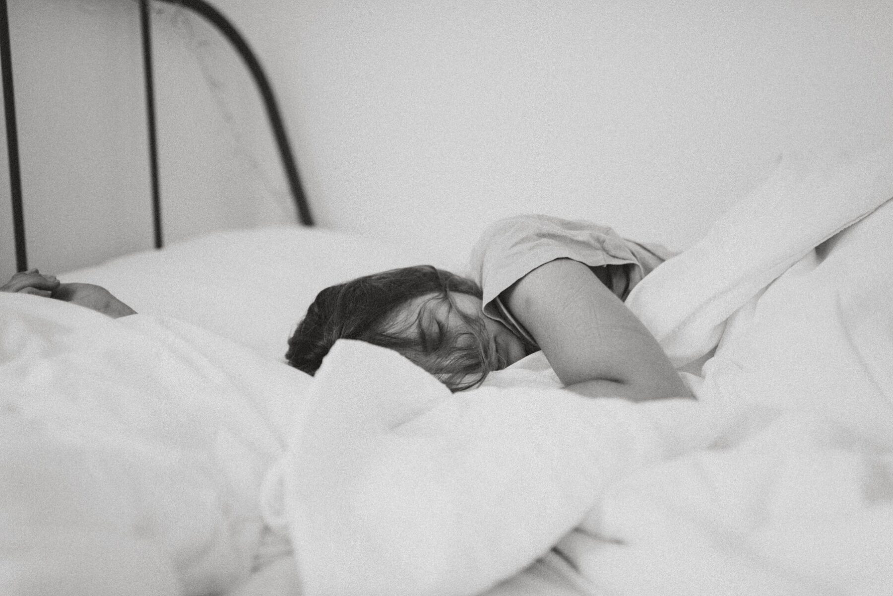 Black and white photo of a dark-haired woman sleeping in a bundle of white blankets in bed.