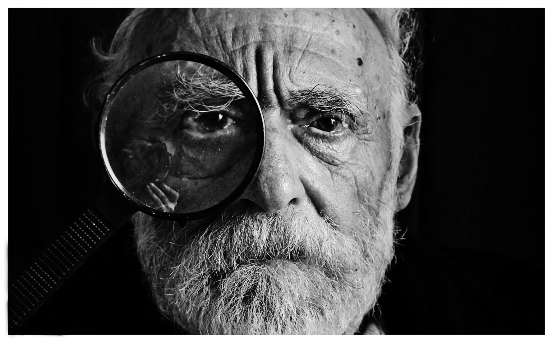 close up facial portait of an elderly gent with a magnifying glass over his eye