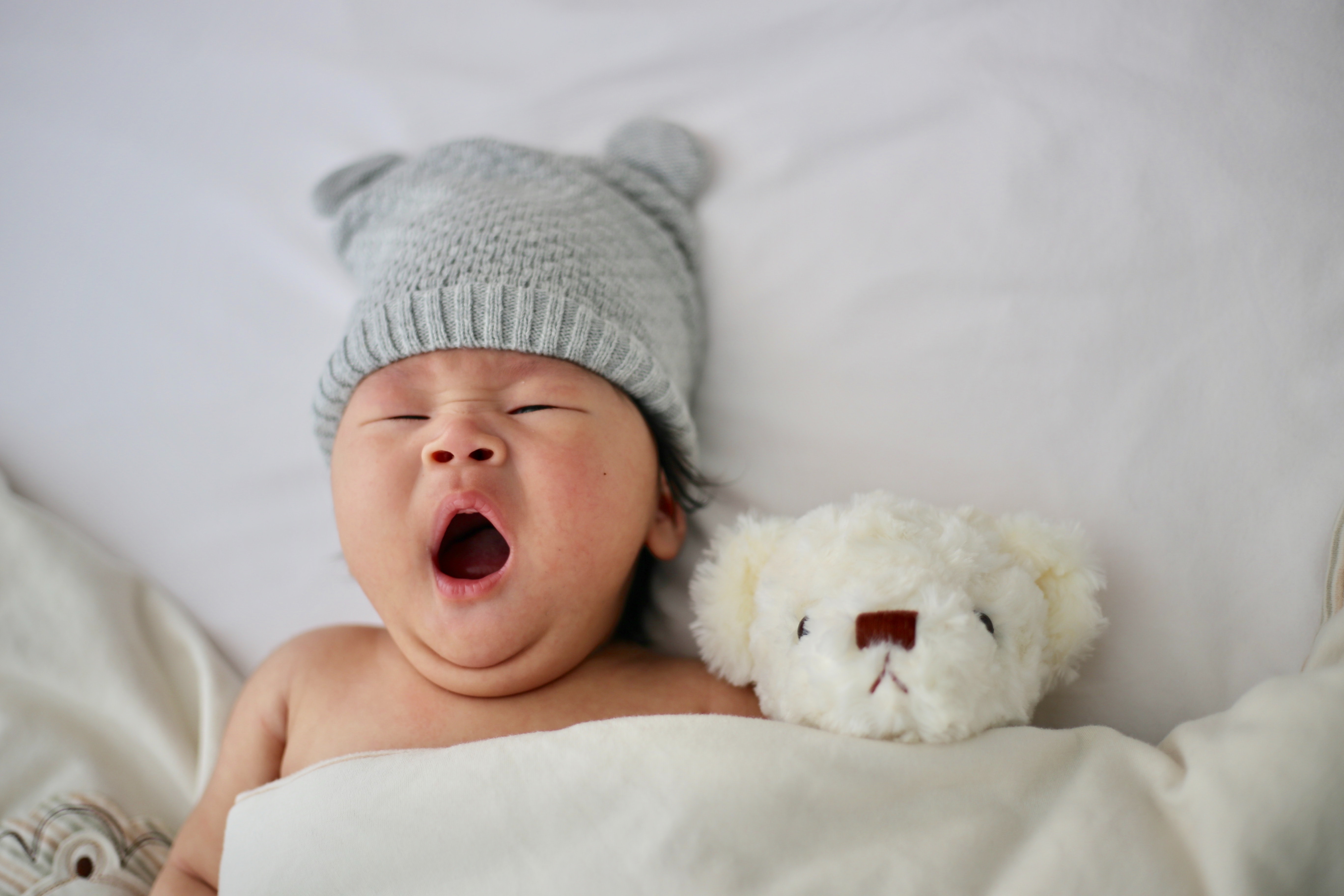 baby yawning next to teddy bear