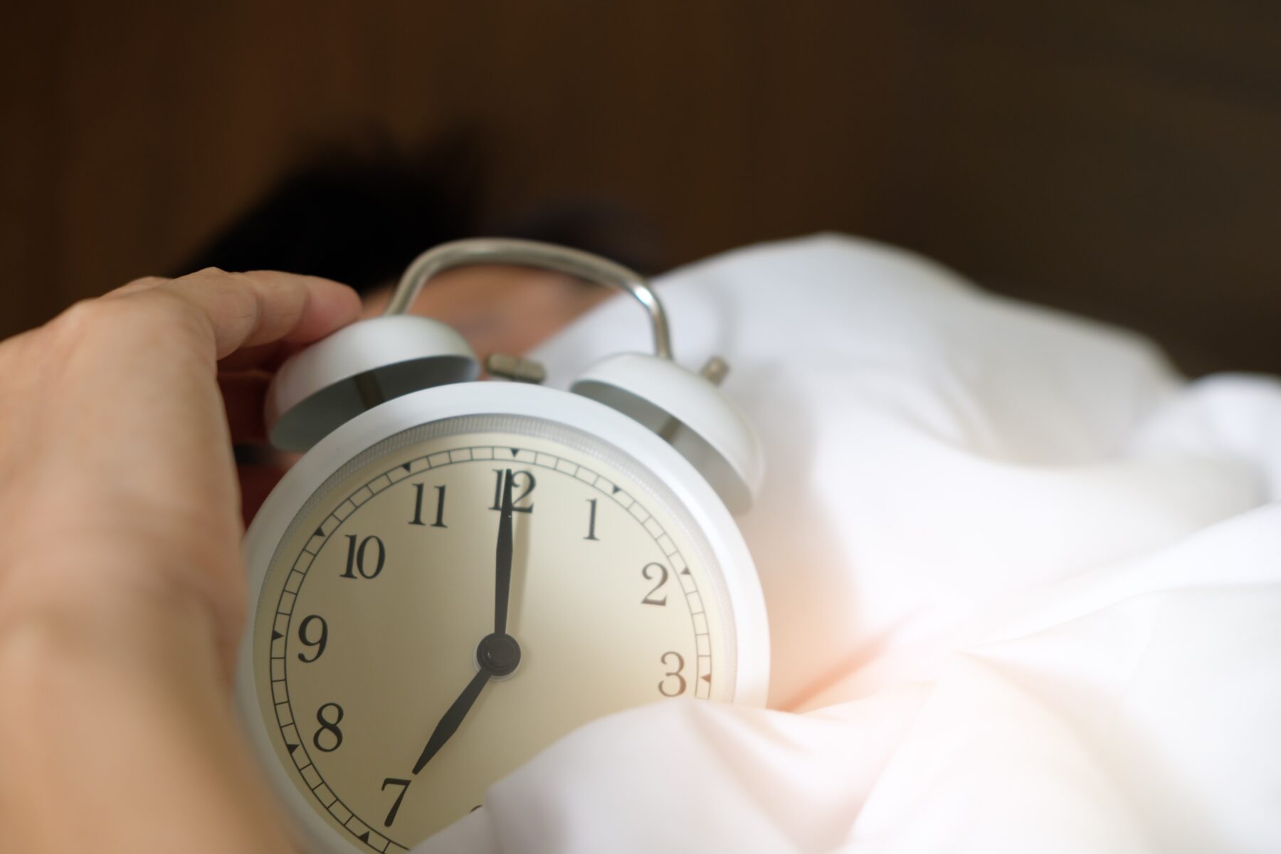 A white clock on a white bed being held still