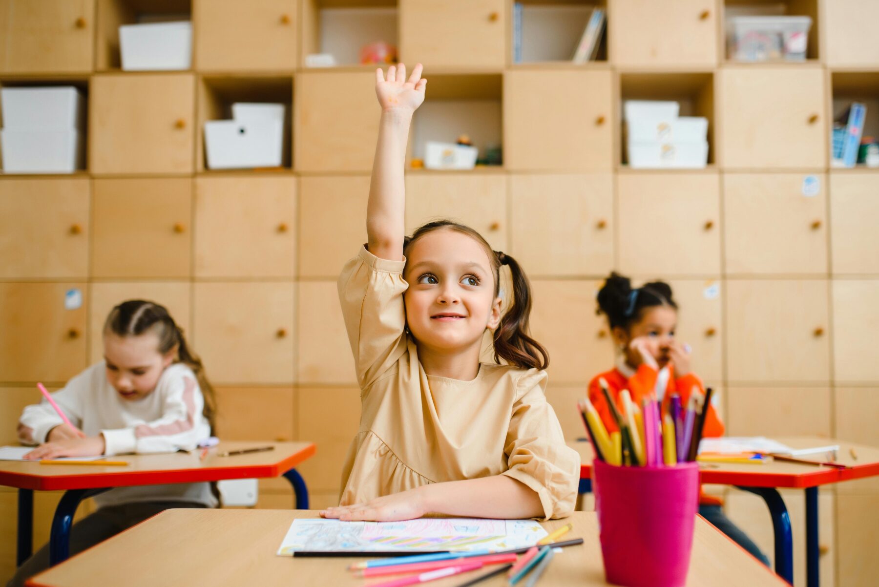 Little girl putting her hand up in school