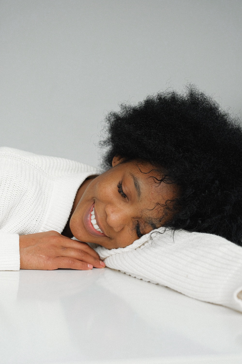 Lady with natural hair sleeping on white bed while smiling