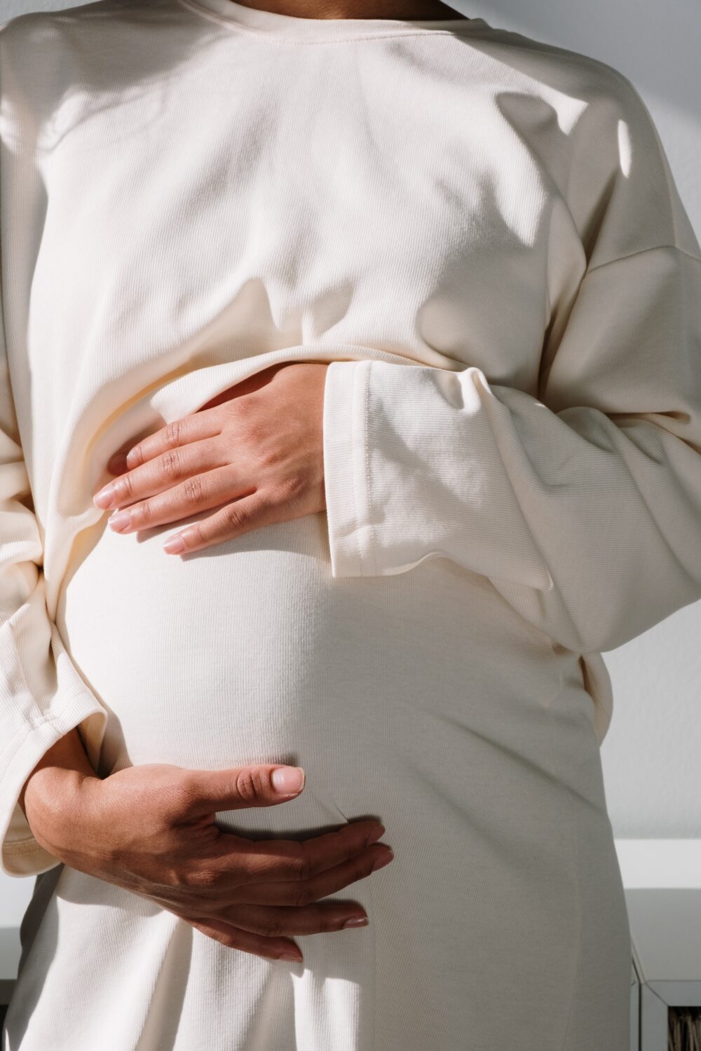 pregnant woman holding their belly with a white dress on, their face not visible