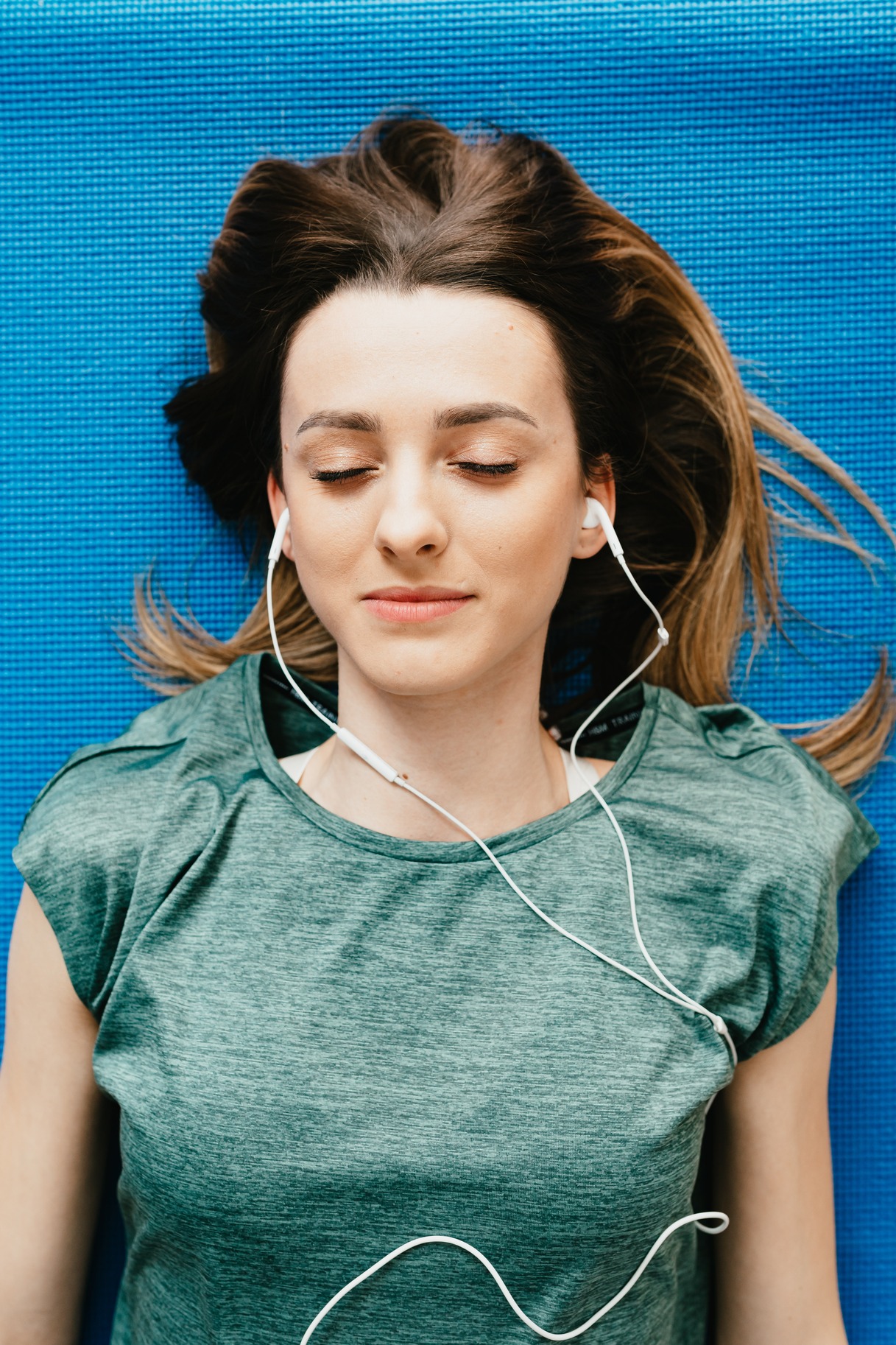 A woman sleeping on a blue background, with earphones in.
