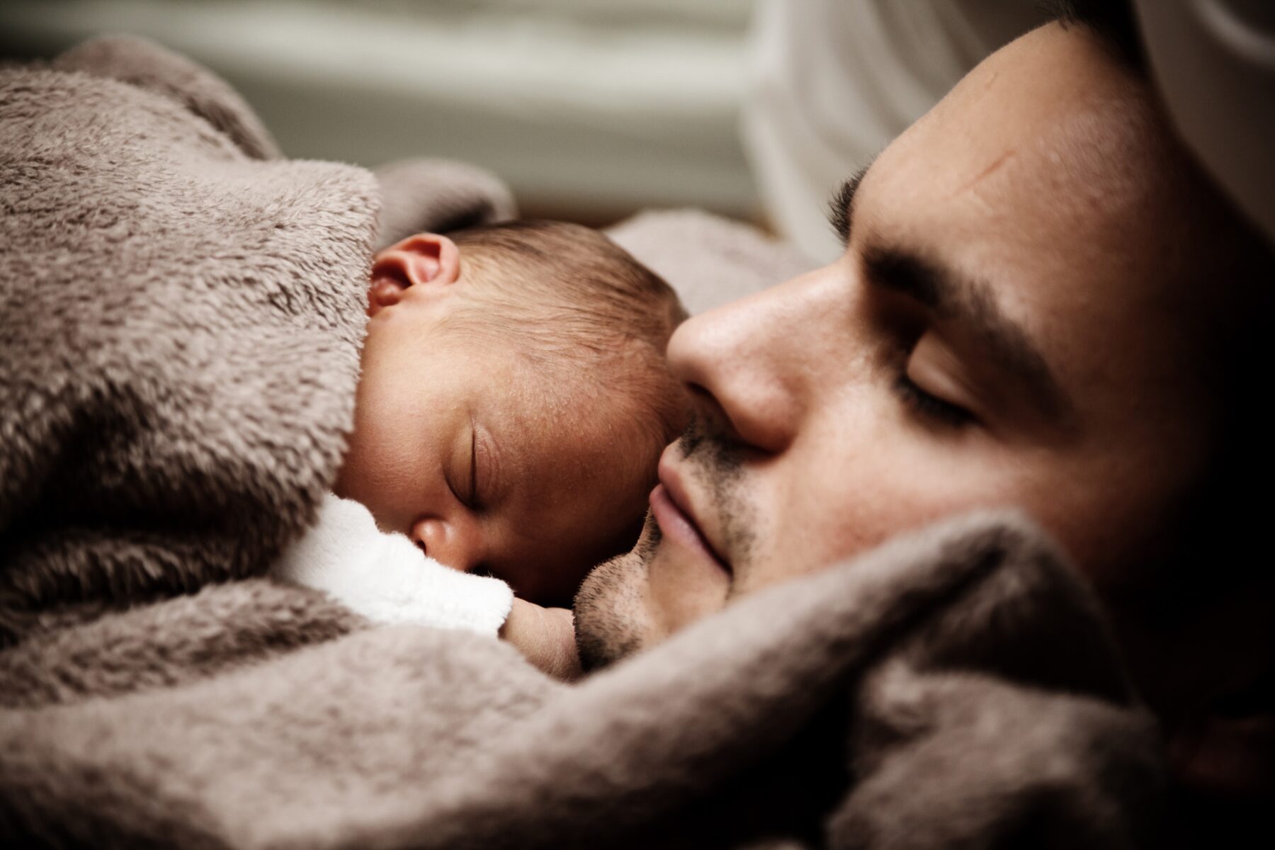A father holds a baby in blankets while the both of them sleep.