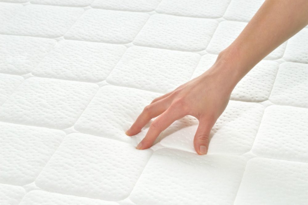 A hand pressing down on a mattress