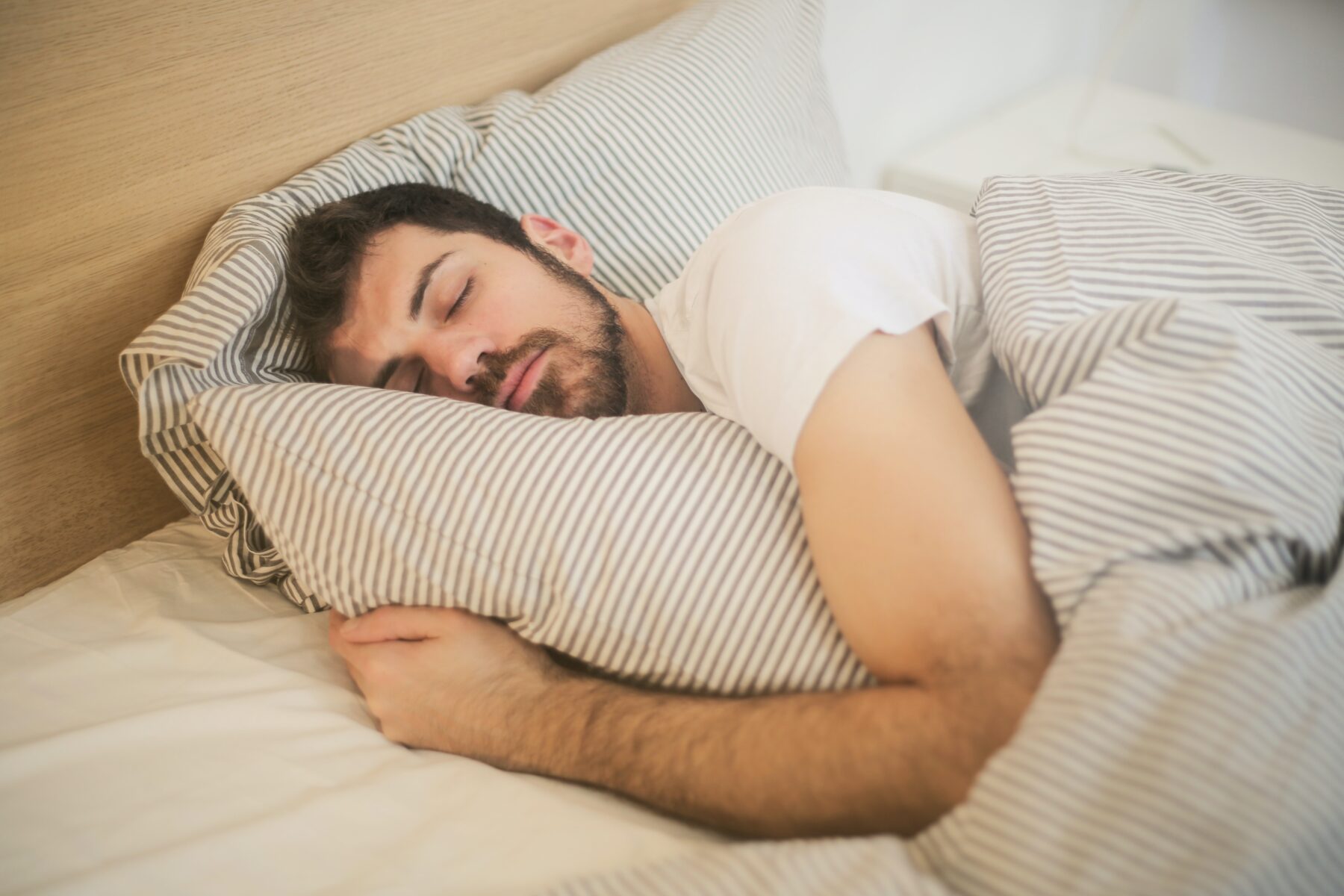 A man sleeping on a wooden bed, hugging the striped duvet.