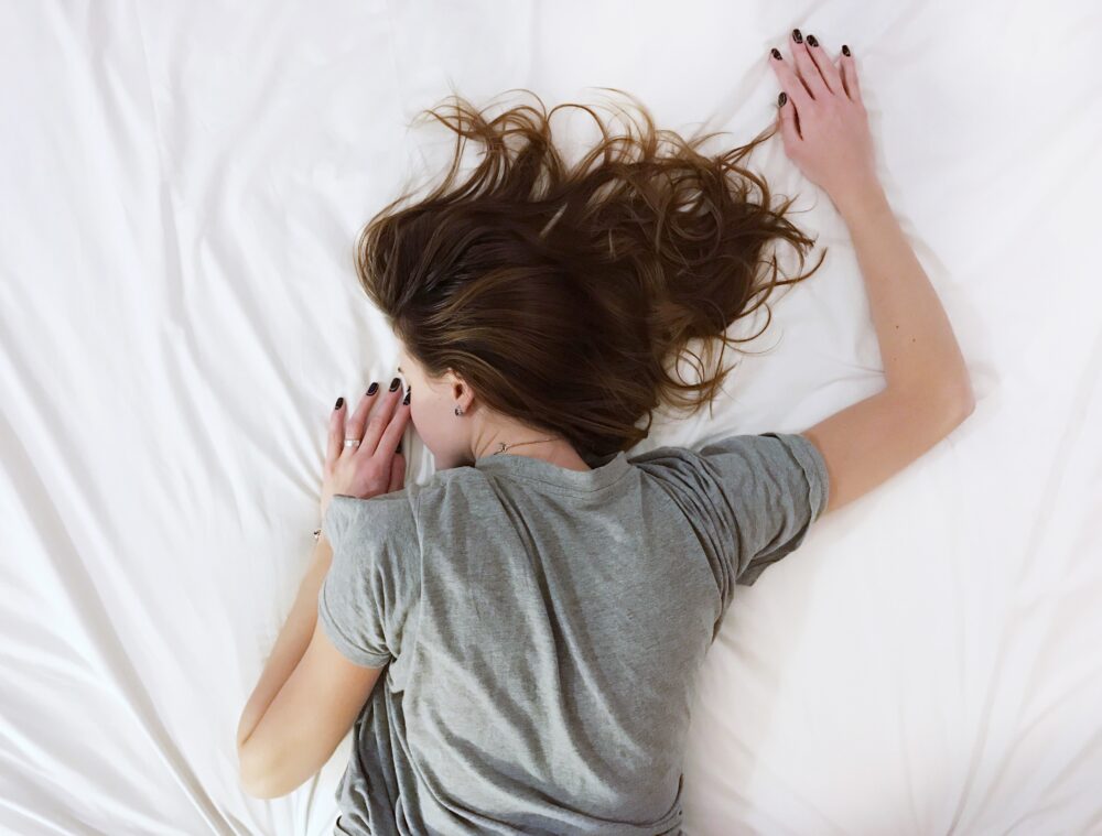 A woman sleeping on a white bedsheet stomach down.