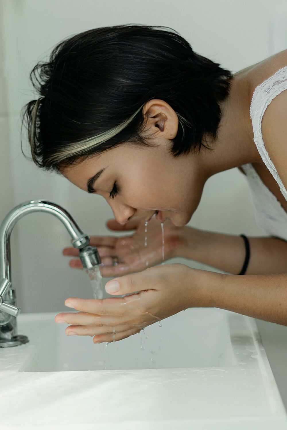 woman splashing face with water over sink