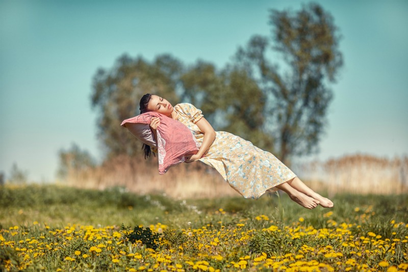 A woman sleeping on a pillow while floating in a field of flowers and grass.